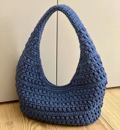 a crocheted blue purse sitting on top of a wooden floor next to a white wall