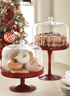 two desserts under a glass dome on top of a table next to a christmas tree