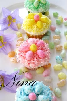 three cupcakes decorated with candy and flowers on a plate