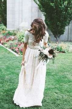 a woman in a white dress is walking through the grass with flowers on her bouquet