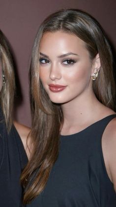 two beautiful young women standing next to each other in front of a brown wall and wearing earrings