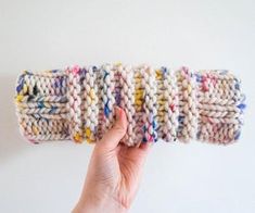 a hand holding up a knitted object with multicolored yarns on it