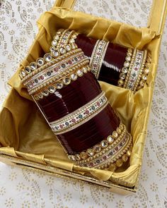 two maroon and gold bangles in a yellow box on a white tablecloth covered table