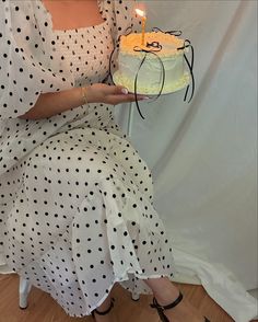 a woman sitting on a chair holding a cake with a lit candle in her hand