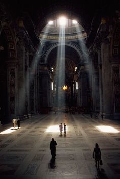 people are walking through an empty church with sunlight streaming in from the ceiling and windows