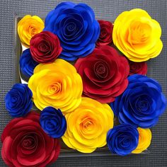 colorful paper flowers are arranged in a square tray on the floor, with one red and one blue flower