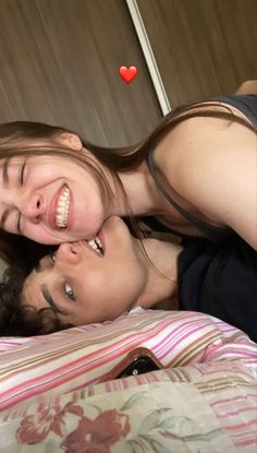 two people are laying on a bed and one is smiling at the camera while the other looks up