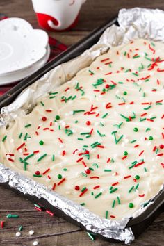 a pan filled with frosting and sprinkles on top of a wooden table