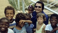 a group of children standing next to each other in front of a man with sunglasses on