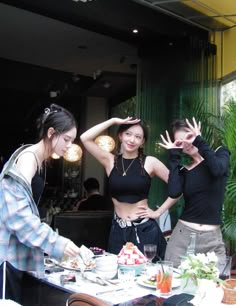 three young women standing around a table with food and drinks on it's plates