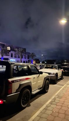 several cars are parked on the side of the road at night with street lights in the background