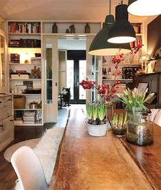 a wooden table topped with potted plants next to a white chair and bookshelf