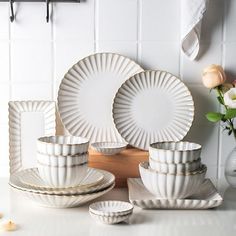 white dishes and cups on a counter with flowers in vases next to the plates