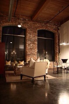 a living room filled with furniture next to two large windows in front of a brick wall