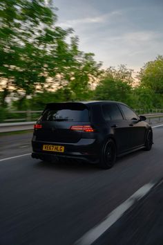 a black car driving down the road with trees in the background