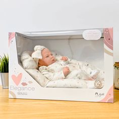 a baby doll in a box on a wooden table next to a potted plant