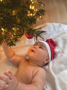 a baby wearing a santa hat laying under a christmas tree