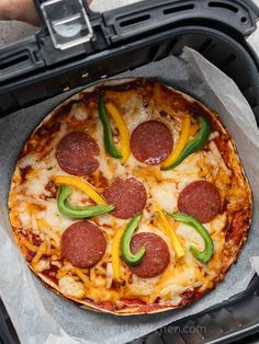 a pizza with pepperoni and green peppers on it sitting in an open grilling pan