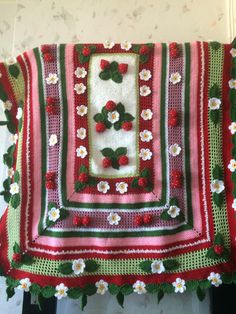 a crocheted blanket with flowers and leaves on the edge is hanging from a wall