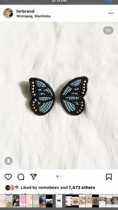 two blue and black butterfly shaped earrings on top of a white fur covered bed with photos