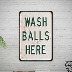 a sign that says wash balls here on the side of a white brick wall next to a potted plant