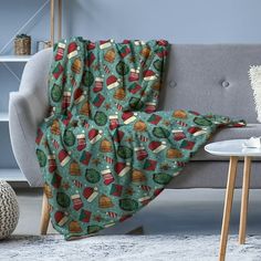 a couch with a blanket that has coffee cups and hotdogs on it next to a table