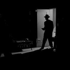 a man in a suit and hat walking into a dark room