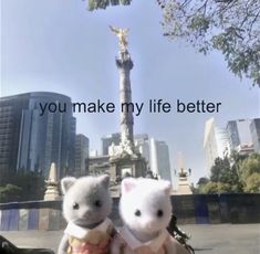 two stuffed animals sitting next to each other in front of a statue with the words you make my life better