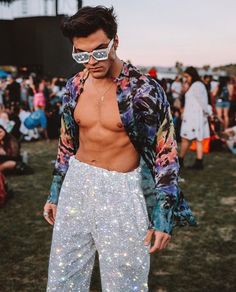 a man with no shirt on standing in front of a crowd wearing disco pants and sunglasses