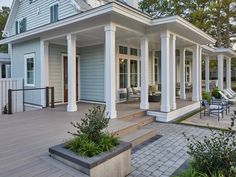 a house with white pillars and blue sidings on the front porch, surrounded by greenery