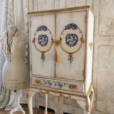 an old white cabinet with blue and gold designs on the doors is next to a mannequin