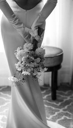 a woman in a long white dress holding a bouquet of flowers and wearing gloves with her hands on her hips