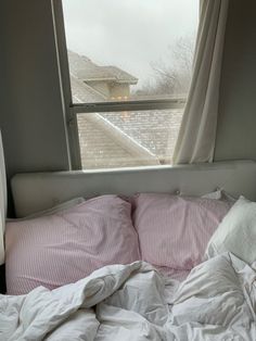 an unmade bed in front of a window with snow on the ground and trees outside