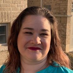 a woman standing in front of a brick building with a green shirt on and red lipstick