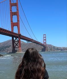 a woman standing in front of the golden gate bridge looking at the water and hills