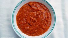 a bowl filled with red sauce on top of a white table cloth next to a spoon