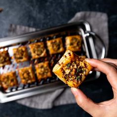 someone holding up some food in front of a metal pan with other food on it