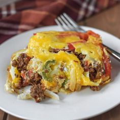 a white plate topped with an enchilada covered in meat and cheese next to a fork