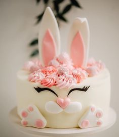 a white cake with pink frosting and bunny ears on it's face is decorated with flowers