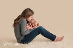 a woman holding a baby in her arms while sitting on the floor next to a rug