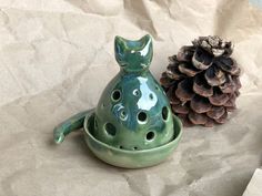 a green ceramic cat sitting next to a pine cone