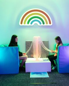 two women sitting on couches in front of a rainbow light