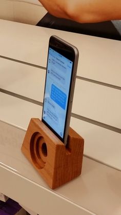 a cell phone sitting on top of a wooden speaker box next to a person's hand