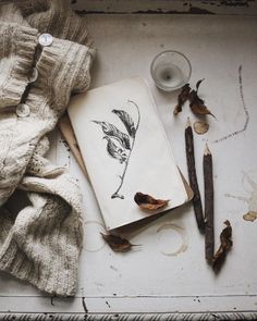 an open book sitting on top of a white table next to some leaves and a candle