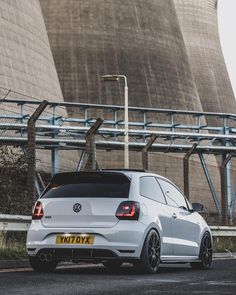 a white volkswagen car parked in front of two large cooling towers on the side of a road