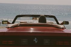 a person is sitting in the back of a red car looking out at the ocean