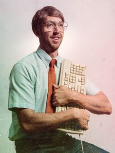 a man with glasses holding a keyboard and smiling at the camera while wearing a tie