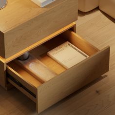 an open drawer on the side of a wooden table with a book and remote control in it