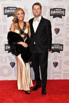 a man and woman in formal wear standing on a red carpet at an awards event