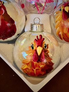 three glass christmas ornaments in the shape of roosters on a white platter with pink and red streamers